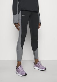 Svarta och grå tajta leggings med en elegant design, som har kontrasterande paneler. Bärs med lavendelfärgade träningsskor.