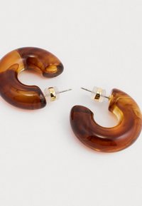 Διάφανα σκουλαρίκια κρίκοι από πορτοκαλί καφέ ακρυλικό με καμπυλωτό σχέδιο, διακοσμημένα με χρυσές λεπτομέρειες και διάφανα πλαστικά στοιχεία.