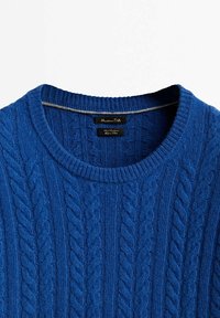 Pull bleu à col rond en maille torsadée avec col côtelé et étiquettes de marque visibles à l'intérieur de l'encolure.