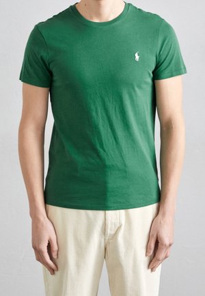 Groene katoenen t-shirt met korte mouwen, ronde hals en een klein wit logo op de linkerkant van de borst. Gecombineerd met lichtgekleurde, gestructureerde broeken.