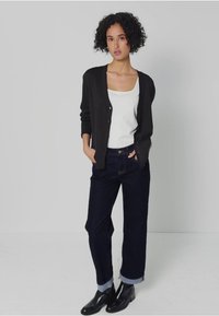 Svart kofta över en vit linne, parat med mörkblå jeans med uppvikta fållar. Bärs med svarta ankelskinn stövlar. Slät yta, enkel design.