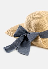 Szeroki kapelusz słomkowy z ciemnoniebieską kokardą z materiału. Kapelusz ma teksturowany, pleciony design oraz naturalny kolor słomy.