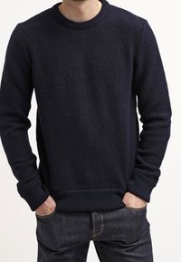 Mörkblå runt halsen tröja i texturerad tyg, med ribbad mudd och nederkant, i en avslappnad passform. Bärs över mörka jeans.