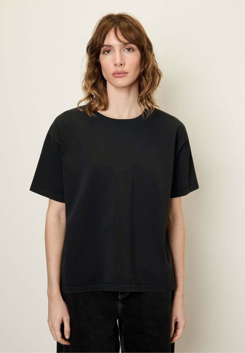 Melnas īsām piedurknēm t-krekls, kas izgatavots no mīksta auduma, ar apaļu kakla izgriezumu un brīvu piegriezumu, savienots ar tumšām džinsām.