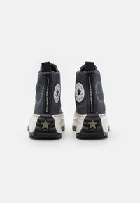 Wysokie sneakersy z ciemnoniebieskiej dżinsu, gumową podeszwą, z kontrastowym logo w kształcie gwiazdy i białymi przeszyciami.