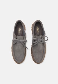 Gray suede shoes with round toe, rubber sole, and gray laces. Features a Clarks logo on the insole, with a textured surface and stylish stitching.