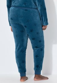 Fleece-pyjamasbukser i mørk teal med stjernemønster. Blød tekstur, elastisk talje og manchetter ved anklerne.