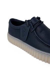 Scarpa di pelle blu navy con punta rotonda, caratterizzata da una superficie testurizzata, suola in gomma leggera a contrasto e un'etichetta in pelle con marchio sul lato.