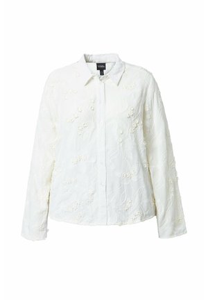 Weißes Hemd mit langen Ärmeln und Knopfleiste, verziert mit floraler, reliefartiger Stickerei und spitzem Kragen vor einfarbigem Hintergrund.