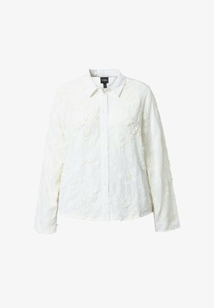 Weißes Hemd mit langen Ärmeln und Knopfleiste, verziert mit floraler, reliefartiger Stickerei und spitzem Kragen vor einfarbigem Hintergrund.