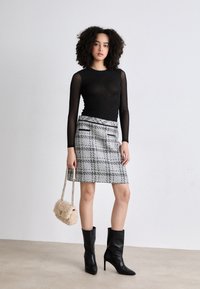 Μαύρη μπλούζα με μακριά μανίκια από δίχτυ, καρό γκρι φούστα με τσέπες, μαύρες δερμάτινες μπότες με τακούνι, και μικρή μπεζ τσάντα από γούνινο ύφ ασμα με αλυσίδα.