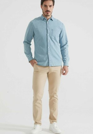Chemise en chambray bleu clair avec un col à boutons, poche poitrine, associée à un pantalon slim beige et des baskets blanches.