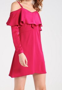 Fuchsia Off-Shoulder-Kleid mit Rüschendetails, langen Ärmeln und einem ausgestellten Saum. Glattes, glänzendes Material mit einer figurbetonten Silhouette.