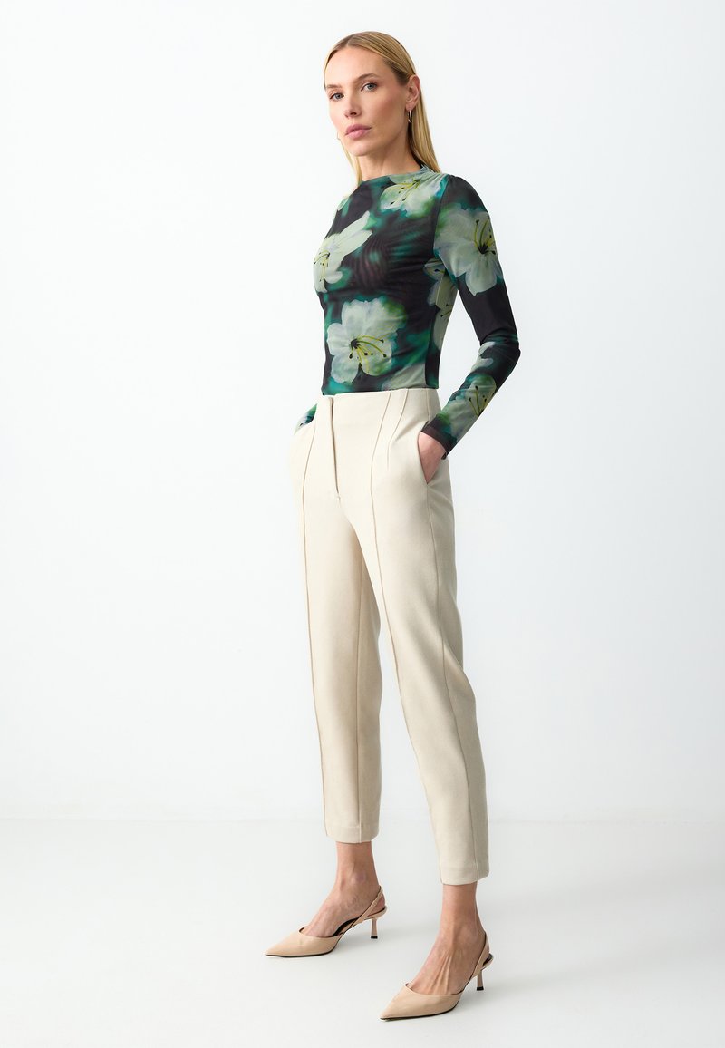 Langemouw T-shirt met een bloemmotief in groen en zwart, gecombineerd met crèmekleurige tapered broek en huidskleurige hakken met een stiletto-ontwerp.