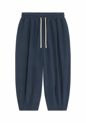Pantalons de survêtement bleu marine avec une taille élastique, cordon de serrage crème ajustable, poches latérales et chevilles fuselées. Texture douce.