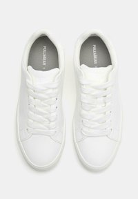 Sneakers bianchi con una tomaia in materiale sintetico liscio, design classico con lacci, collare imbottito e soletta grigia texturizzata con branding.
