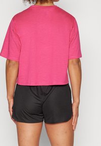 Camiseta corta rosa hecha de tejido suave, con mangas cortas y cuello redondo, combinada con pantalones cortos deportivos negros.