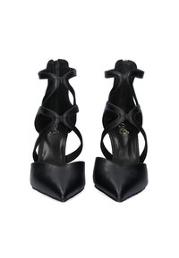 Zapatos de tacón alto negros hechos de cuero suave. Presentan punta puntiaguda, lados abiertos con correas cruzadas y una cremallera en la parte trasera.