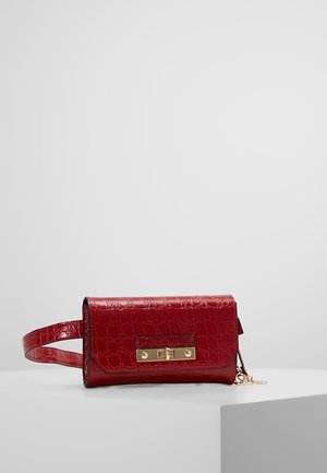 Czerwona torebka na pasku z imitacji skóry krokodyla, z prostokątną złotą klamrą i regulowanym paskiem, umieszczona na białej powierzchni.