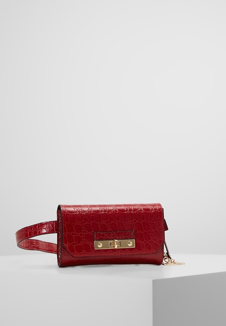 Riñonera de cuero sintético rojo con textura de cocodrilo, hebilla rectangular en tono dorado y correa ajustable, colocada sobre una superficie blanca.