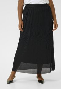 Jupe maxi plissée noire avec une taille large, dotée d'une couche transparente et d'une silhouette évasée, associée à des chaussures noires à bout pointu.