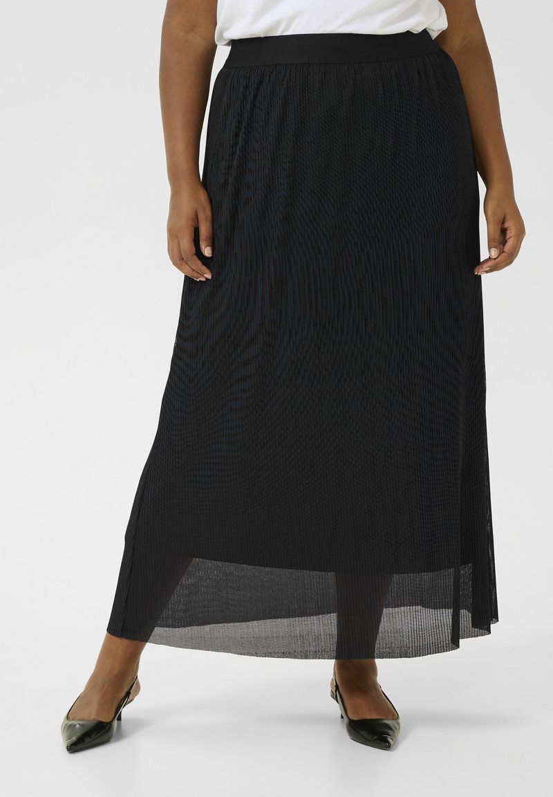 Jupe maxi plissée noire avec une taille large, dotée d'une couche transparente et d'une silhouette évasée, associée à des chaussures noires à bout pointu.