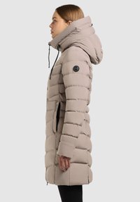 Beige puffer jacket met een hoge kraag, een geblokt patroon, zijzakken en een logopatch op de linkerarm. Glad textuur, middellange uitvoering.