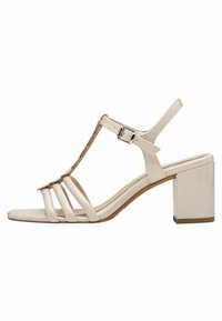 Sandales à talon beiges avec un design en T, de multiples lanières, un bout carré et un talon bloc. Fabriquées en matériau synthétique lisse.