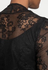 Zwarte kant kleding met complexe bloempatronen en een doorschijnende textuur. Het ontwerp heeft een gaasachtige basis en een zachte stof.