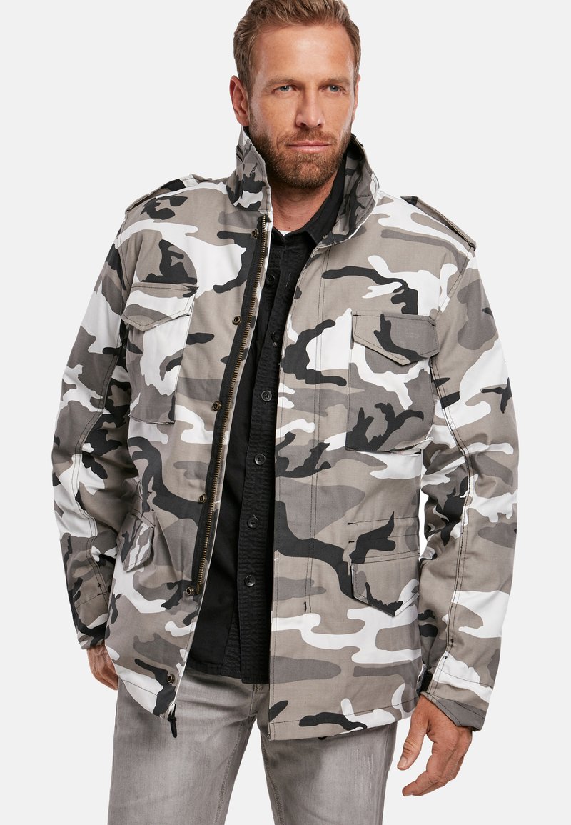 Chaqueta de camuflaje en tonos de gris y negro. Cuenta con múltiples bolsillos, un cuello alto y un cierre frontal con cremallera. Tejido texturizado.