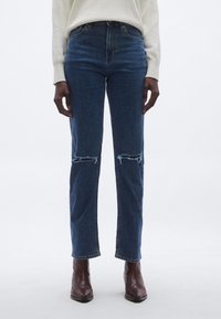 Sinised teksad kõrge vöökohaga, millel on kulunud põlvenooled, sirged sääred ja klassikaline viiepusega disain.