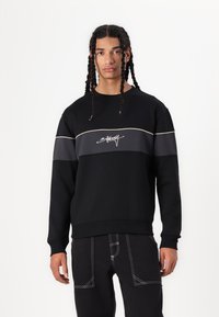 Sudadera negra con una franja horizontal gris y un logo de color claro, con un corte relajado, puños acanalados y dobladillo.