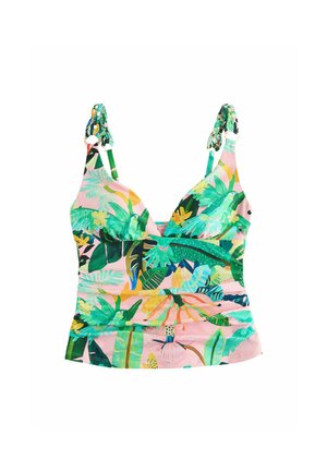 Młoda kobieta w kolorowym bikini z tropikalnym wzorem stoi przy drewnianym drogowskazie na plaży pod przejrzystym niebem z drzewami w tle.