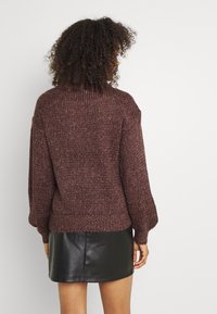 Brauner gestrickter Pullover mit strukturierter Optik und Ballonärmeln, kombiniert mit einem schwarzen Leder-Minirock, von hinten betrachtet.