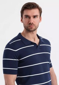 Námorně modrá polokošile s krátkým rukávem, která se vyznačuje bílými vodorovnými pruhy, límečkem a přiléhavým střihem. Texturovaná látka se subtilním brandingem.