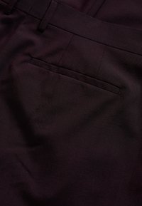 Sötétlila nadrág, sima textúrával, slim fit szabással, övhurkokkal és egy hátsó zsebbel.