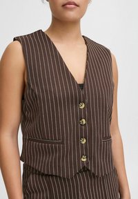 Gilet marron à rayures avec un décolleté en V prononcé, six boutons dorés et deux poches avant. Le tissu a une texture lisse.