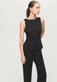 Haut noir sans manches avec un design structuré, comprenant un ourlet à basque. Le tissu semble lisse et opaque, associé à un pantalon assorti.