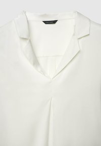 Camicia bianca con scollo a V, colletto corto e un sottile dettaglio di piega sul davanti. Realizzata in tessuto liscio e leggero.