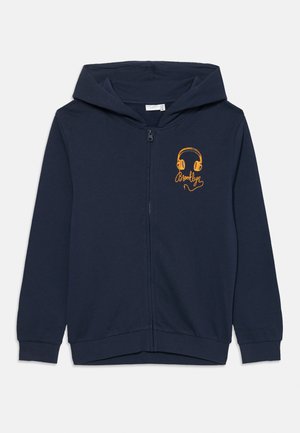 Temno modra zip-up kapuca iz mehkega materiala, s sprednjim zadrgo, kapuco in rumeno grafiko slušalk z napisom "Brooklyn".