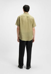 Korte mouwen, olijfgroene linnen shirt met een relaxte pasvorm. Kenmerken een klassieke kraag en verlaagde schouders, gecombineerd met zwarte broeken.