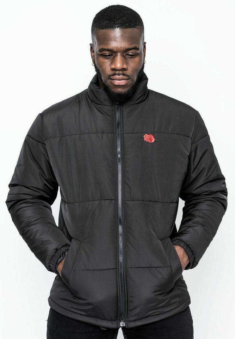 Svart vadderad jacka med hög krage, dragkedjestängning och röd ros broderi. Har sidofickor och en slät, glänsande finish.