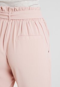 Ljust rosa byxor med draperad elastisk midja, har en bakficka och sidoflikar, tillverkade av ett mjukt tyg.