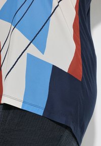 Top de manga corta con un patrón geométrico en azul, rojo, blanco y marino, con tejido suave y un corte relajado en el dobladillo.