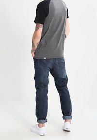 Gray t-shirt with black shoulder accents, paired with rolled-up dark blue jeans and white sneakers. Textured fabric and casual fit.