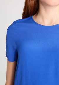 Top blu corto a maniche corte realizzato in un tessuto liscio e leggero, con colletto rotondo e una texture sottile, adatto per un abbigliamento casual.