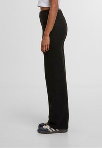 Černé široké pletené kalhoty s vysokým pasem. Hladká textura, dlouhý design. V kombinaci s modro-bílými skládacími botami.