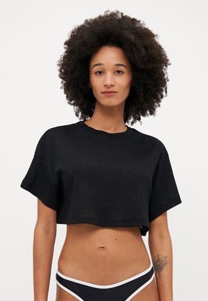 Avkortad svart T-shirt i textilmaterial med struktur, med korta ärmar och vid halsringning, bärs över svarta bikiniunderdelar med vit kant.