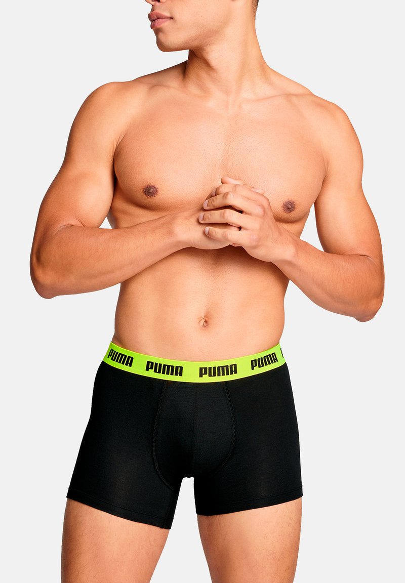 Schwarze Boxer-Slips mit einem neongrünen Bund, der "PUMA" in schwarzer Schrift zeigt. Der Stoff wirkt glatt und sitzt eng an.