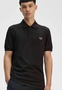 Polo negra hecha de mezcla de algodón, con un cierre de tres botones y un pequeño logotipo bordado en el lado izquierdo del pecho. Mangas cortas.